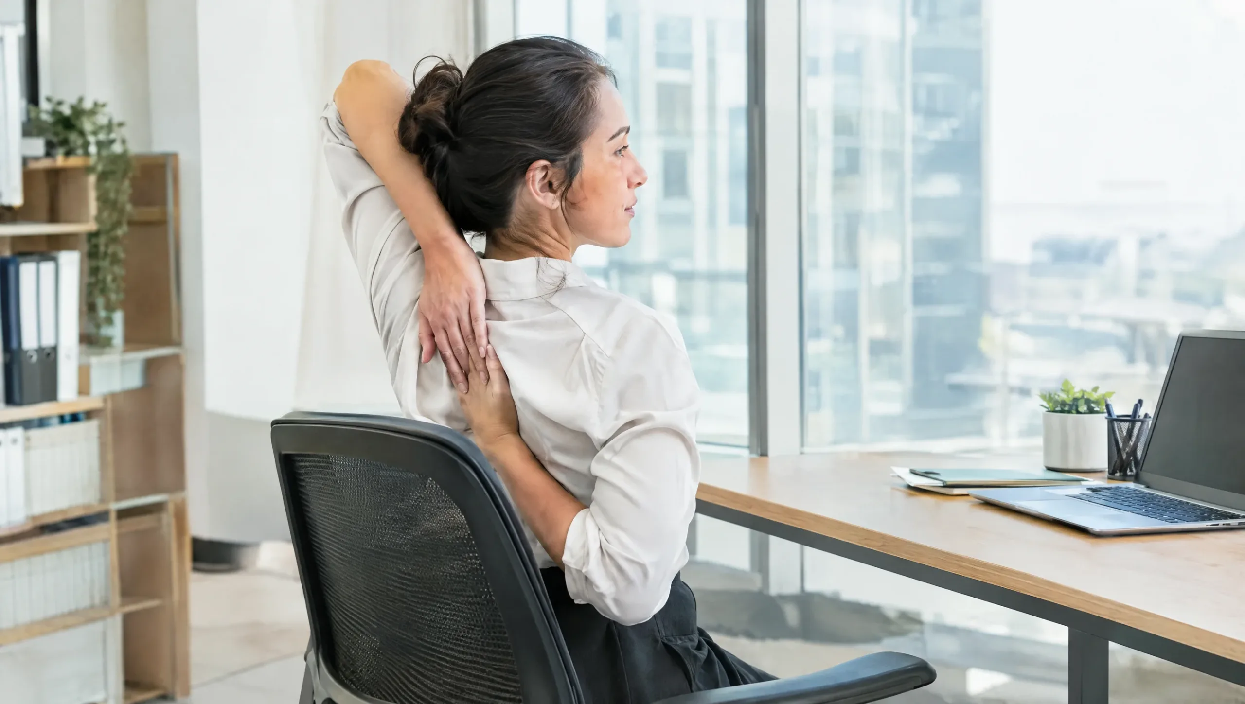 Office worker doing a seated shoulder blade stretch at their desk