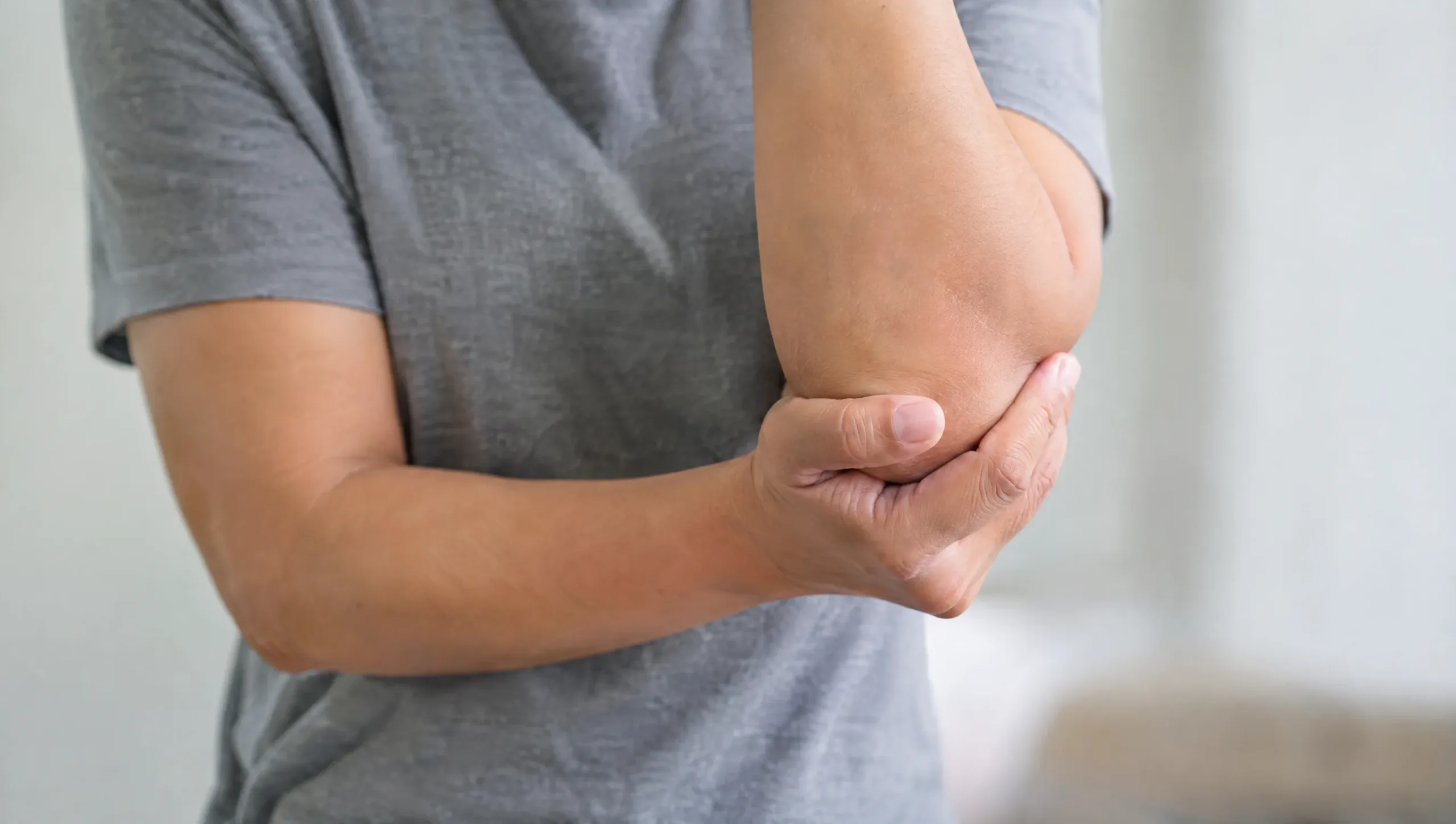 Person holding their elbow in discomfort representing tennis elbow and golfers elbow pain